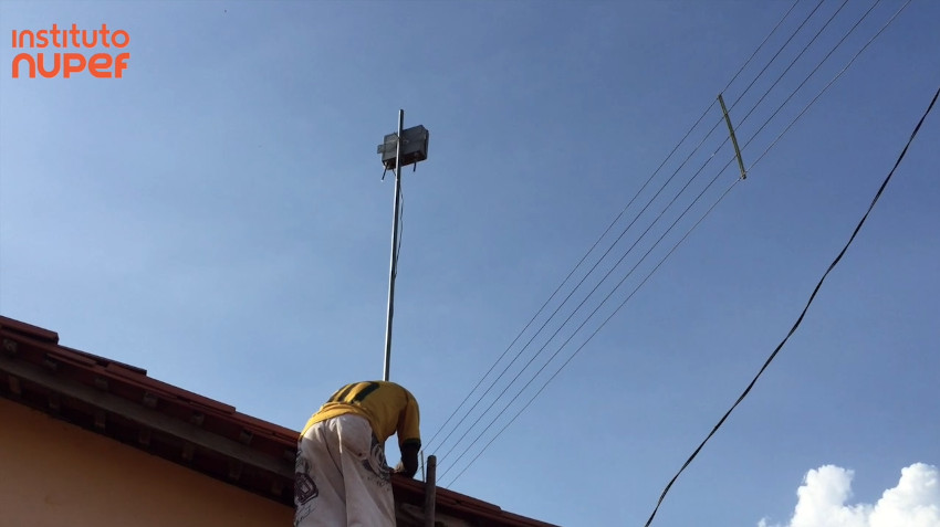 na imagem podemos ver um homem fixando um equipmaneto no telhado de uma casa. Registro feito em um dos projetos de redes comunitárias do Nupef.