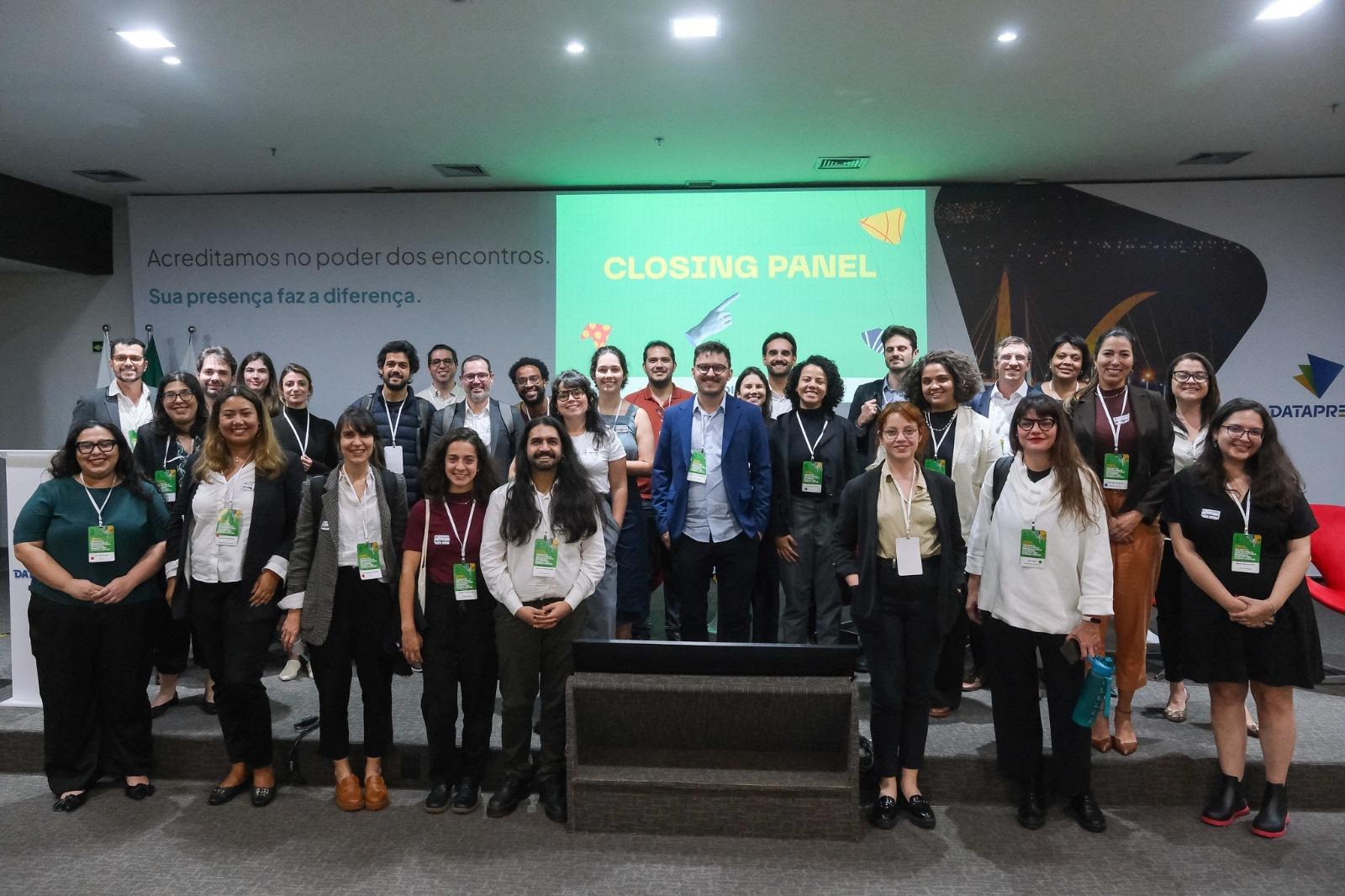 Nessa imagem podemosa ver todos os participantes de pé,posando para a foto, em frente ao painel de apresentação.