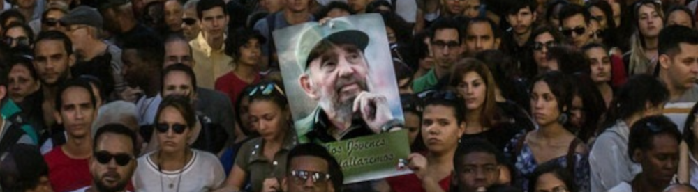 Imagem de uma multidão. Ao centro podemos ver um cartaz com a imagem de Fidel Castro